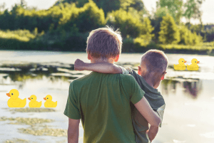 Older boy holding younger boy overlooking pond with ducks 