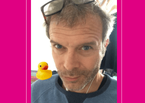 A picture of James Osborne with with a small plastic duck on his shoulder - Pink background