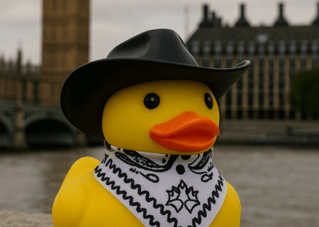 A yellow plastic duck dressed in conwboy gear in front of the house of commons
